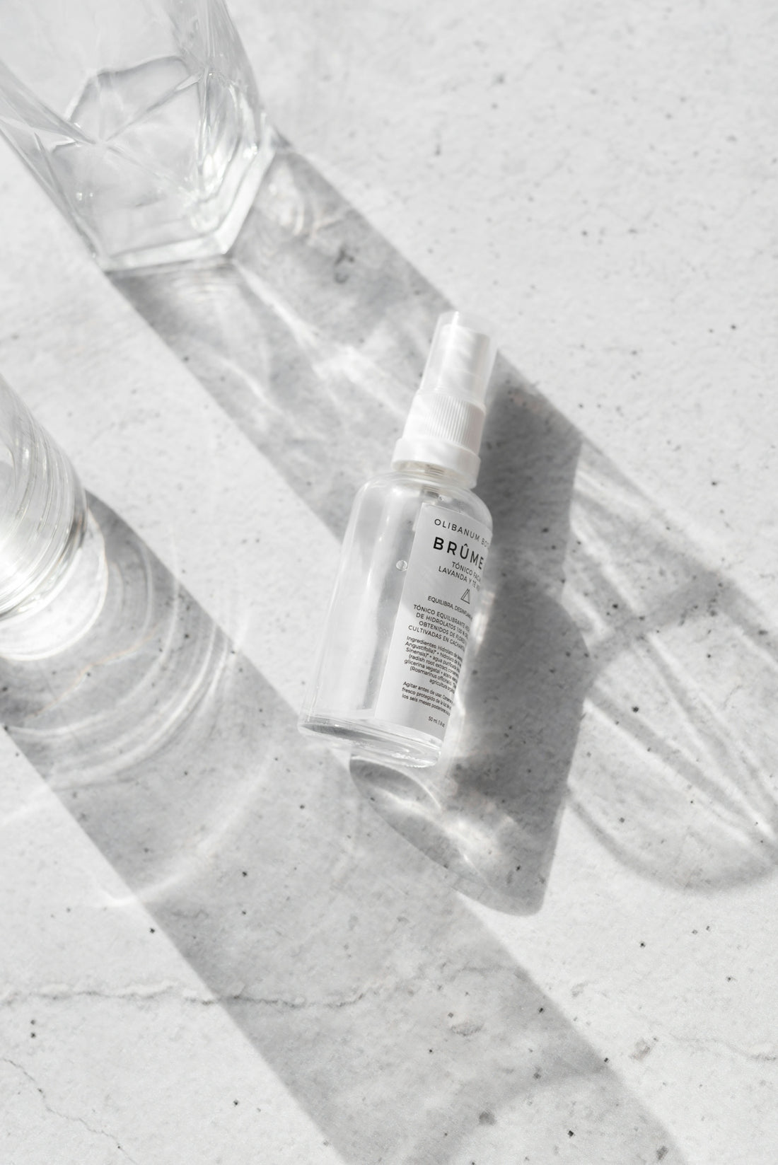 Clear skincare serum bottle with glass of water casting shadows on white surface for Popular Skincare Myths & The Truths Behind Them