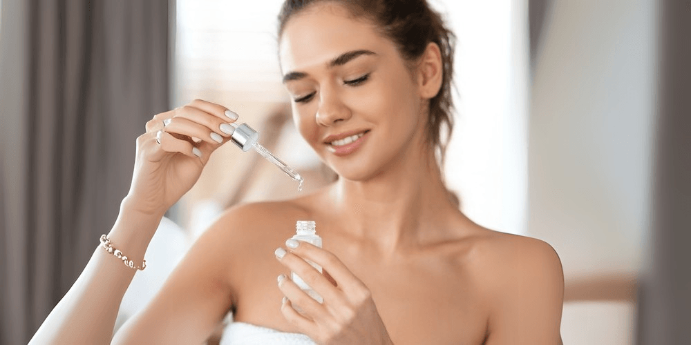 Clear serum bottle with dropper held by a smiling woman with long hair