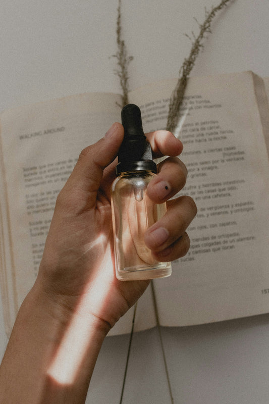 Hand holding a clear glass dropper bottle over an open book for Editorial Navigating The Complex Skincare Market